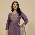 Woman wearing a purple traditional outfit with a matching dupatta on a beige background